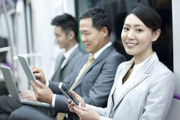 Business persons using digital products in subway train