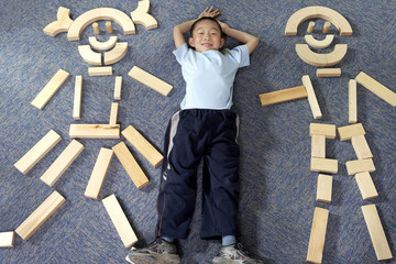 Boy Lying Down On Floor Next To Wooden Shapes