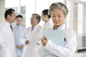 Senior Doctor in Forground with Clipboard, Doctors and a Nurse in Background