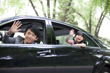 Cheerful father and daughter waving out of car window