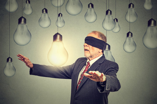 Blindfolded senior man walking through light bulbs searching for bright idea