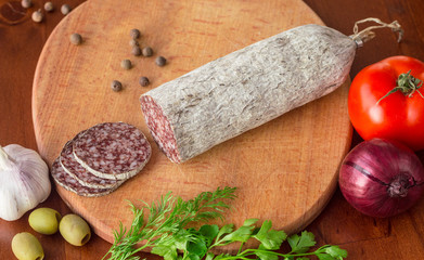 Hungarian salami with vegetables on cutting board on wooden table