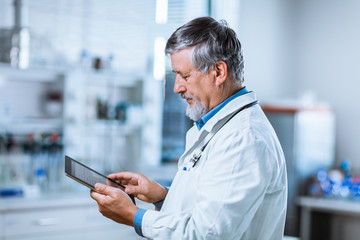 Senior doctor using his tablet computer at work 