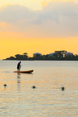 Man silhouette rowing standng on a boat at sunset time.