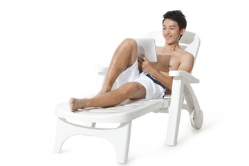 Young man using digital tablet on sand chair