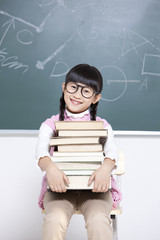 Humorous little girl with textbooks in classroom