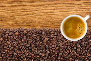 Close-up of roasted coffee beans and cup coffee over wooden back