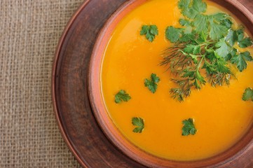 Pumpkin Soup; a bowl of pumpkin soup with bundle of greens and slices of bread