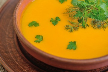 Pumpkin Soup; a bowl of pumpkin soup with bundle of greens and slices of bread