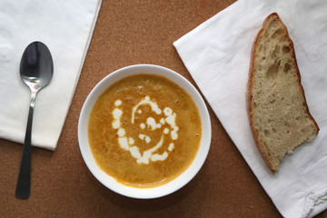 Carrot and onion creamy soup with bread, spoon and white napkins. Cork background. Top view. 