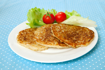 A  potato pancakes with lettuce and tomatoes on a white plate