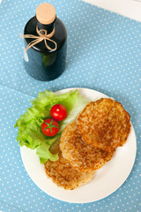 potato pancakes and a bottle of olive oil on blue cloth, top view