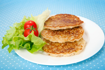 A plate with potato flapjacks, green salad and cherry tomatoes