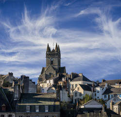 Fototapeta na wymiar La ville Quimperlé en Bretagne avec l'église Saint Michel devant un ciel avec des nuages cirrus