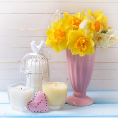 Yellow narcissus in vase, candles  and decorative heart on blue