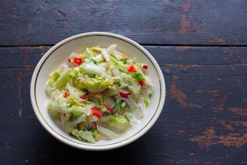 Vegetable salad made of fresh cabbage, radish, cucumber, bell pepper and sour cream in a white plate on an old black table. Top view closeup. Copy space. Free space for text
