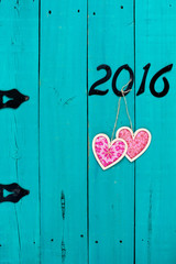 Year 2016 in black iron numbers and pink hearts hanging on wooden door