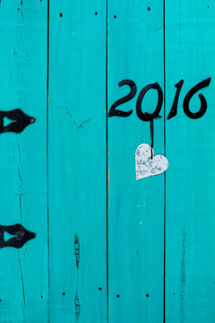 Year 2016 in black iron numbers and silver tin heart hanging on wooden door