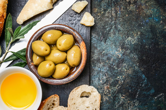 Olives appetizer with cheese, oil and ciabatta gut slices on dark rustic background, top view, place for text. Italian food
