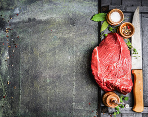 Fresh raw meat with herbs,spices and butcher knife on rustic background, top view, place for text. Cooking concept. Horizontal.