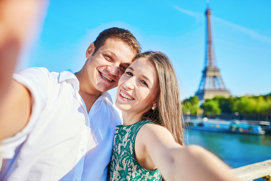Young romantic couple taking funnyselfie with mobile phone near the Eiffel tower in Paris, France