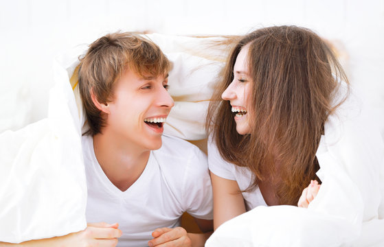 Happy couple laughing in bed peeking out from under blanket