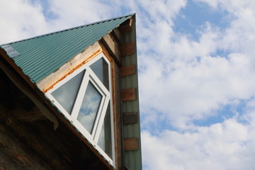 Triangular skylight of an attic of a village log house under construction against a cloudy sky