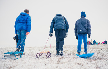 boys dragging sleds on winter snowy hill