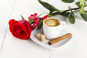 Cup of coffee, red rose, sugar and cinnamon on a white wooden ba