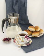 breakfast composition with a cup of tea, jar of milk, cranberries, spoon and pastries