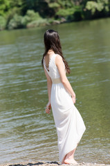 Beautiful young woman wearing a long white dress, standing side by the river