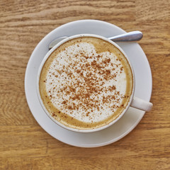 Cappuccino in white cup close-up on wood background