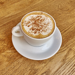 Cappuccino in white cup close-up on wood background