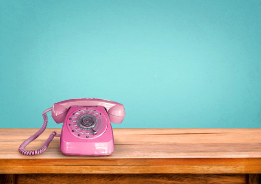 Old retro pink telephone on table with vintage green pastel background