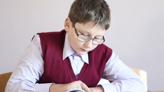 boy with glasses reading a book while sitting at a desk