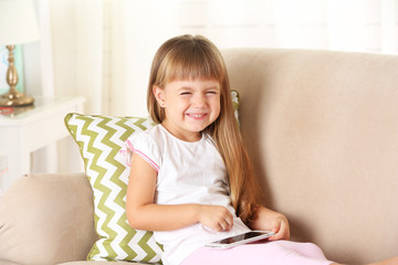 Beautiful little girl  with smart phone sitting on sofa, on home interior background