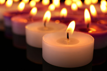 Many burning small candles on dark background, close-up