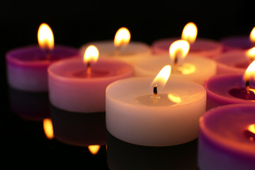 Many burning small candles on dark background, close-up