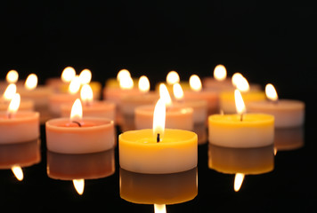Many burning small candles on dark background, close-up