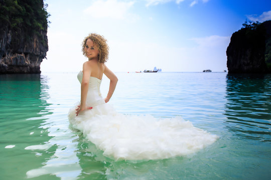 side view blonde bride in fluffy dress in shallow azure sea