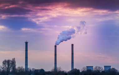 Industrial cityscape with coal power plant and smoke stacks, profiled on sunset sky