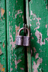 Shabby padlock on an old wooden street door with cracked green paint