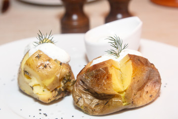 Baked potato is on the plate with sour cream and dill.