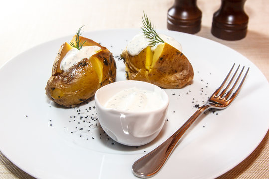 Baked potato is on the plate with sour cream and dill.