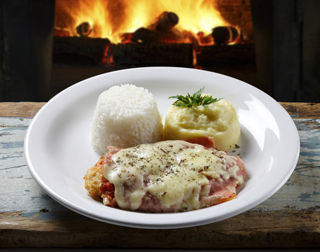 The steak parmigiana with potato and rice with fire in the background