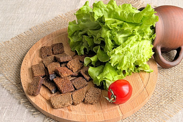 Small rye bread croutons.  Small rye bread croutons on a wooden plank and fresh lettuce leaves in a ceramic mug on a background of burlap.
 