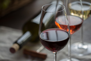 three wineglasses with red, rose and white wine with bottle on brown wood textured table covered with canvas towel