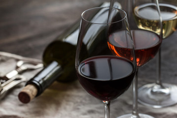 three wineglasses with red, rose and white wine with bottle on brown wood textured table covered with canvas towel