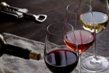 Red, rose and white wine bottles with three wineglasses, grapes and figs on brown wood textured table covered with canvas towel