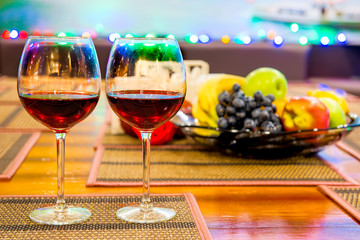 two glasses of red wine on the table near vase with fruit